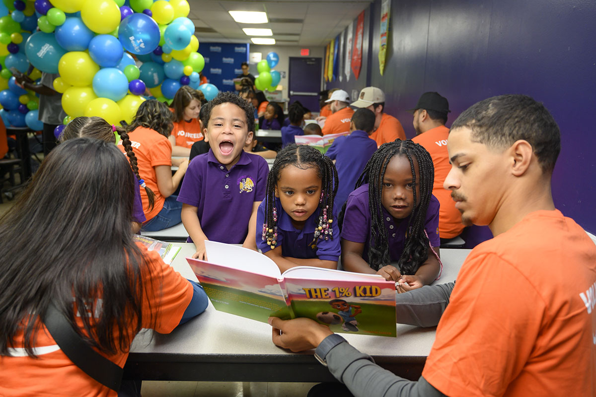 Three kids looking at a book with event volunteers